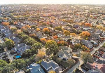 Aerial drone view urban sprawl in suburban Dallas, Texas during fall season with colorful leaves. Flyover subdivision with row of single-family detached houses and apartment complex